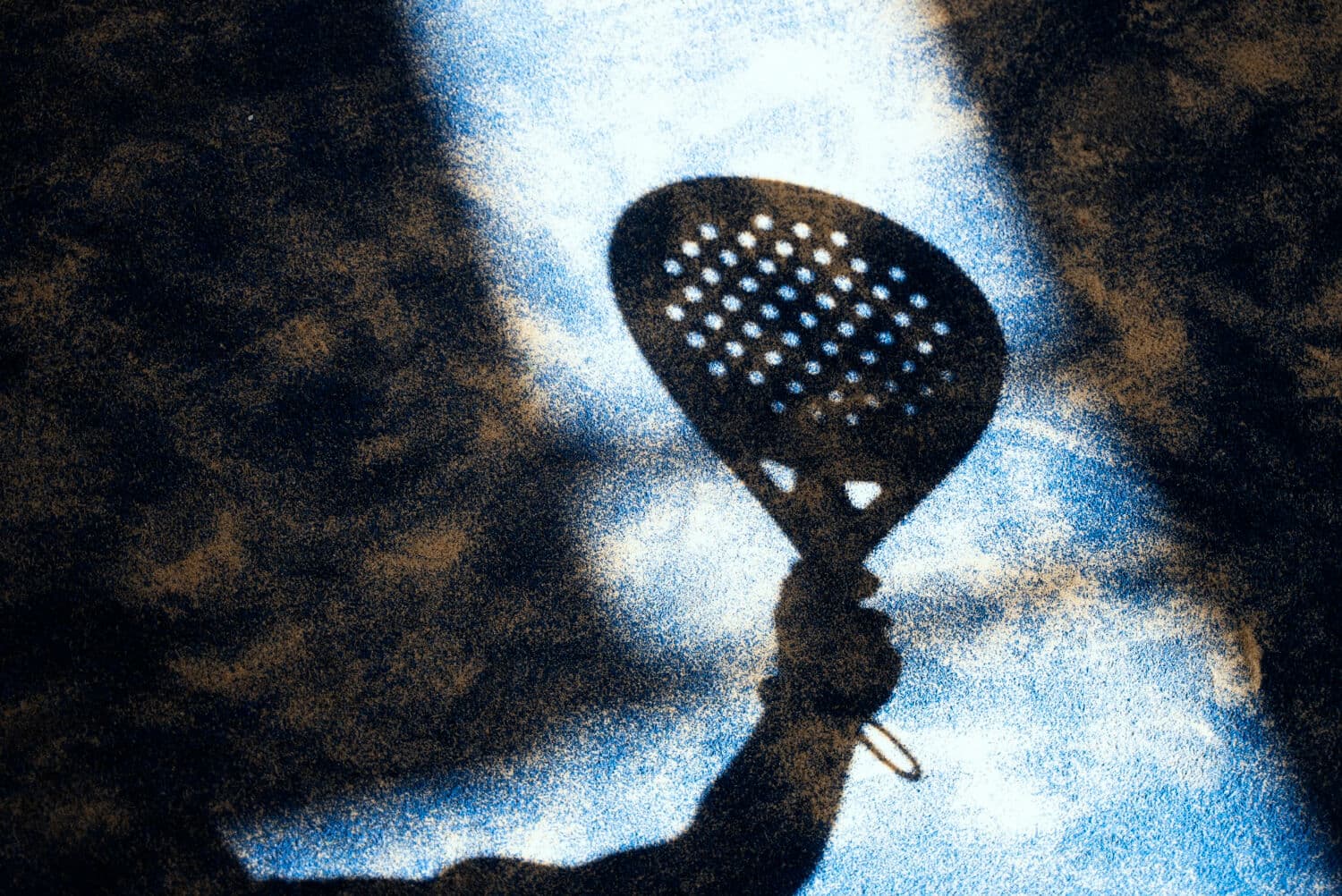 A padel racket held up against dappled light